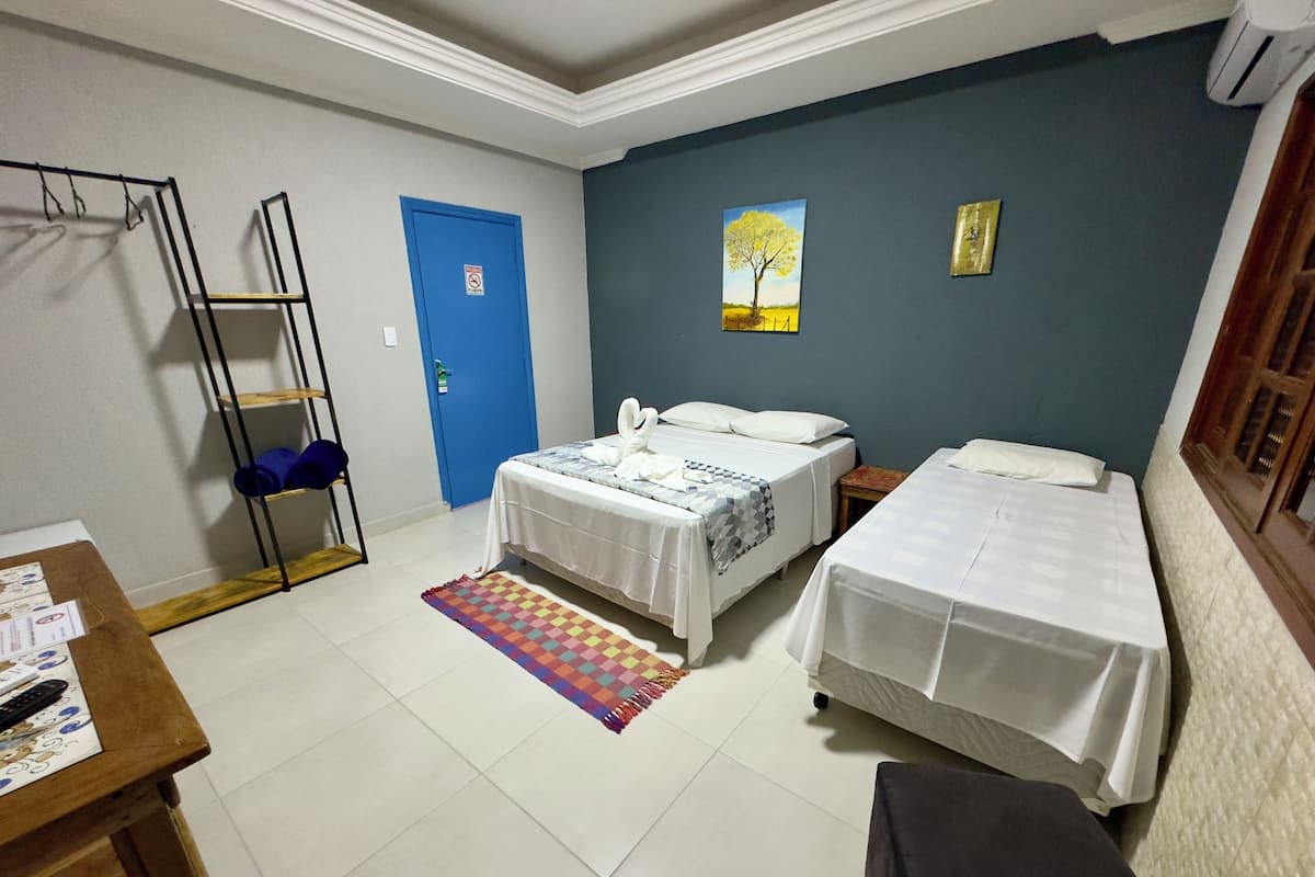 A hotel room with two beds, a desk, a chair, a colorful rug, a blue door, and a painting on the wall.