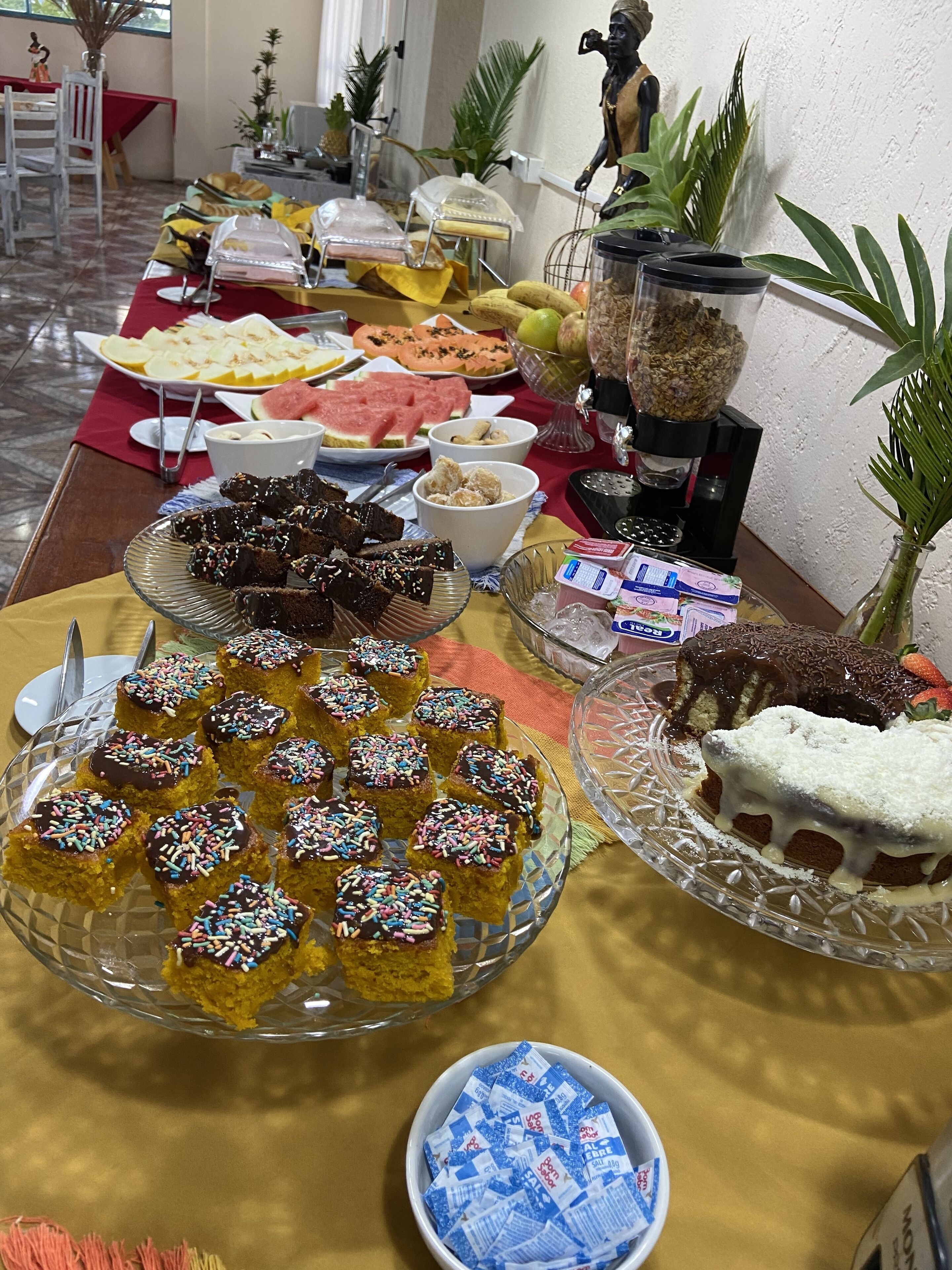 Una mesa de buffet con diversos alimentos, entre ellos pasteles, frutas y aperitivos.