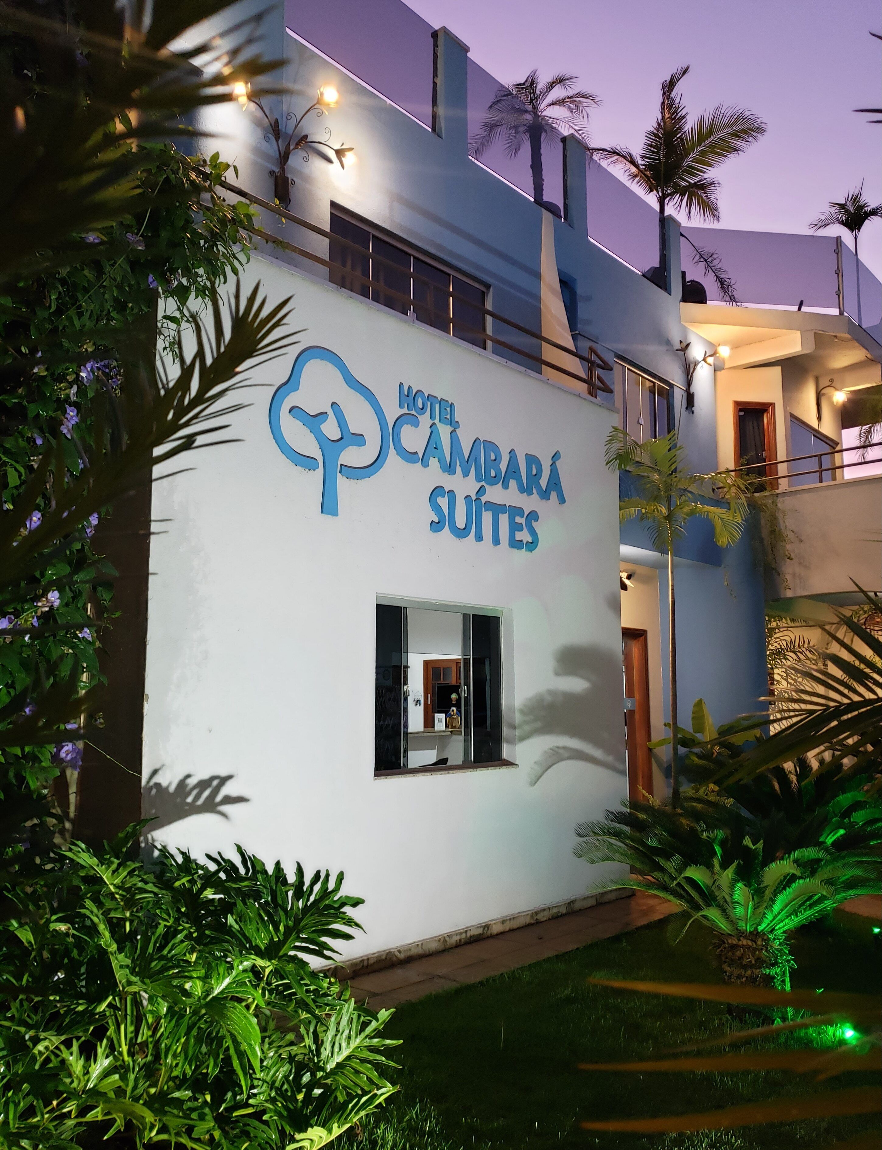 Un hotel con diseño moderno llamado 'Hotel Cambará Suites', que cuenta con un balcón y un ventanal pequeño.