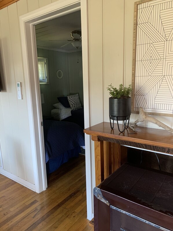 A room with a bed, a potted plant, and a geometric wall art piece. - Cheerful Port Austin Cottage, short walk to the Beach! (Port Austin)