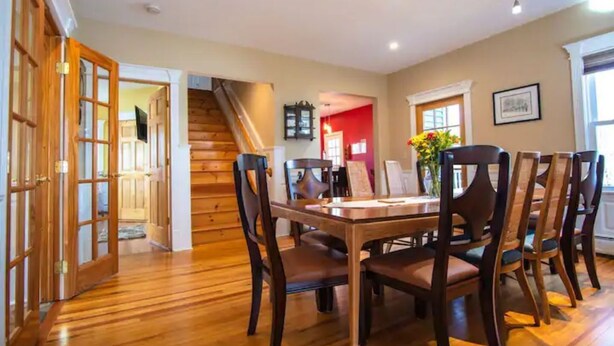 Un comedor con mesa y sillas de madera, una escalera y una pared roja.
