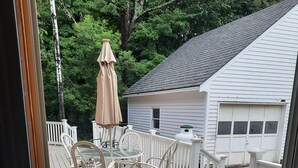 Una terraza de madera con una mesa y sillas, una cerca blanca y una casa al fondo.