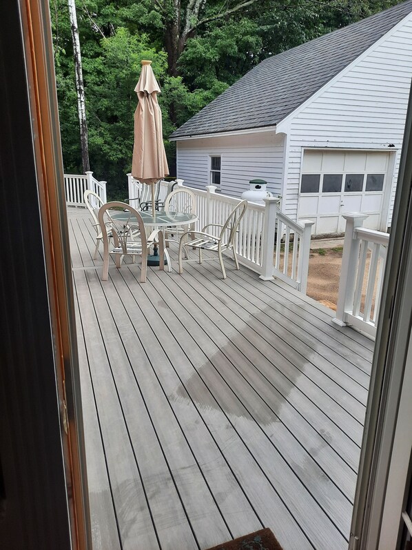 A wooden deck with a table and chairs, a white fence, and a house in the background.