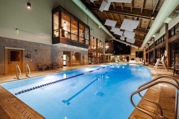 An indoor swimming pool with clear lane dividers, a wooden ceiling, and a view of the upper floor with seating areas.