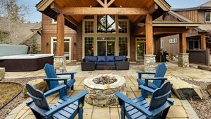 Un área de estar al aire libre con techo, sillas tipo Adirondack, una chimenea de piedra y un jacuzzi.