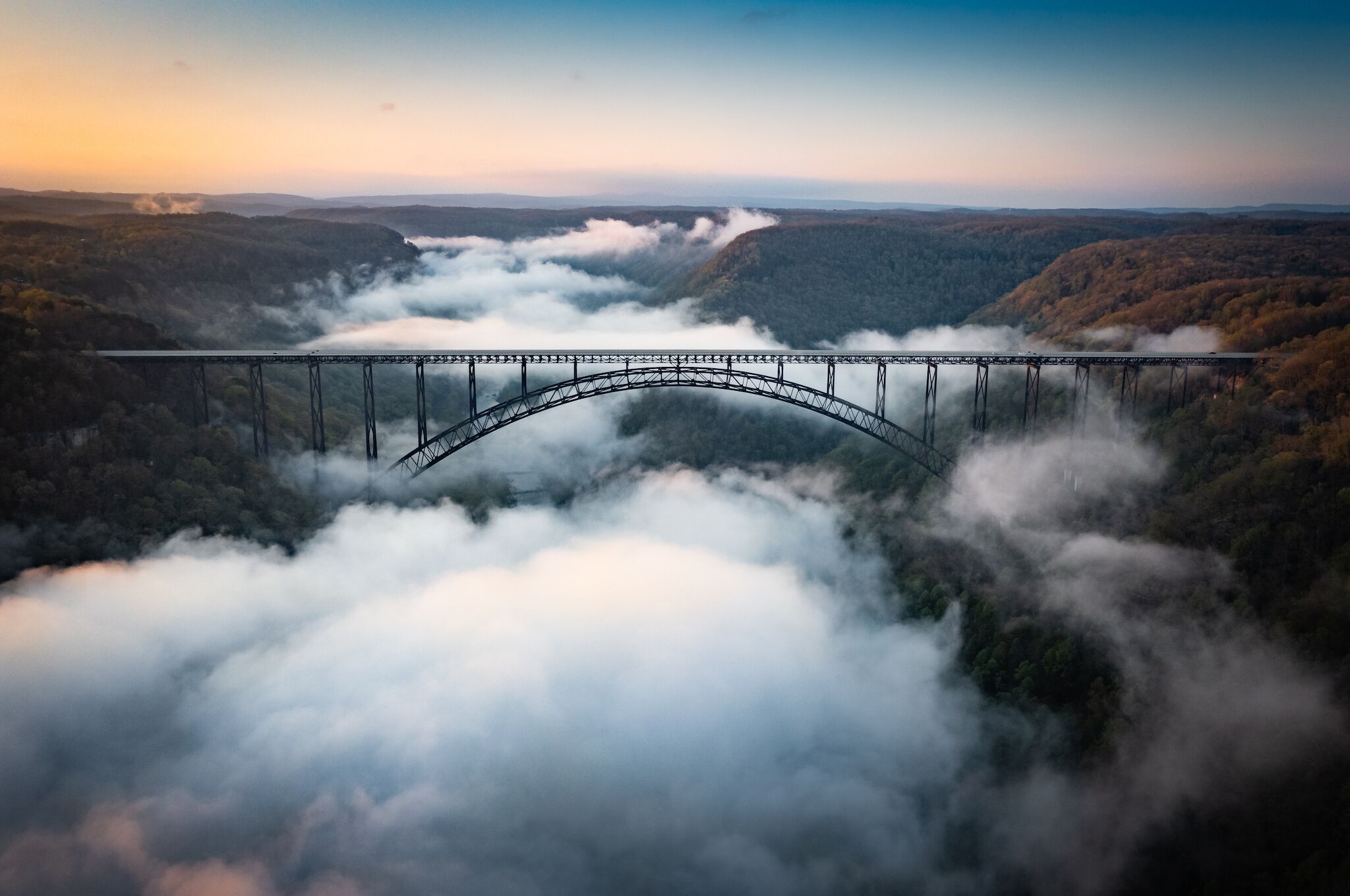 Un puente cruza un valle con bosque denso y niebla.