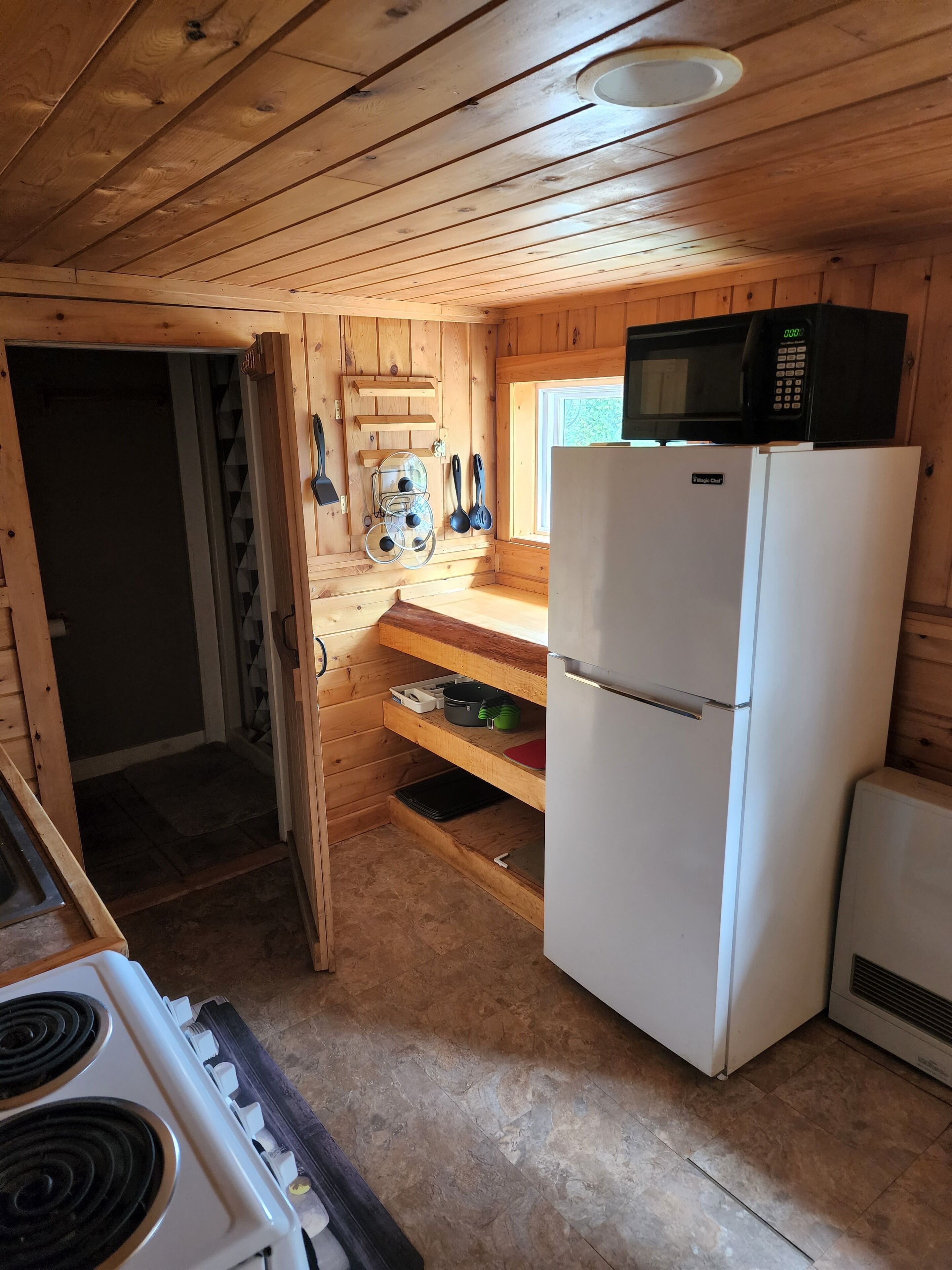 Una cucina compatta con pareti in legno, un fornello bianco, un frigorifero e un forno a microonde.