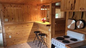 A wooden cabin-style kitchen with a stove, sink, and bar stools. - 1 Bedroom house with direct trail access (Errol)