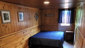 A small, wooden-furnished room with a bed, a window with curtains, and a wall-mounted sign. - 1 Bedroom house with direct trail access (Errol)