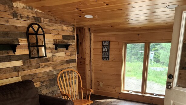 A cozy room with a wooden floor, a brown leather sofa, a rocking chair, and a window with a view of greenery. - 1 Bedroom house with direct trail access (Errol)