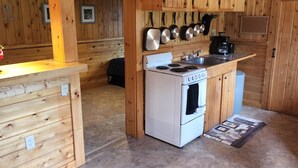 A wooden cabin interior with a kitchen area featuring a stove, oven, and hanging cookware. - 1 Bedroom house with direct trail access (Errol)