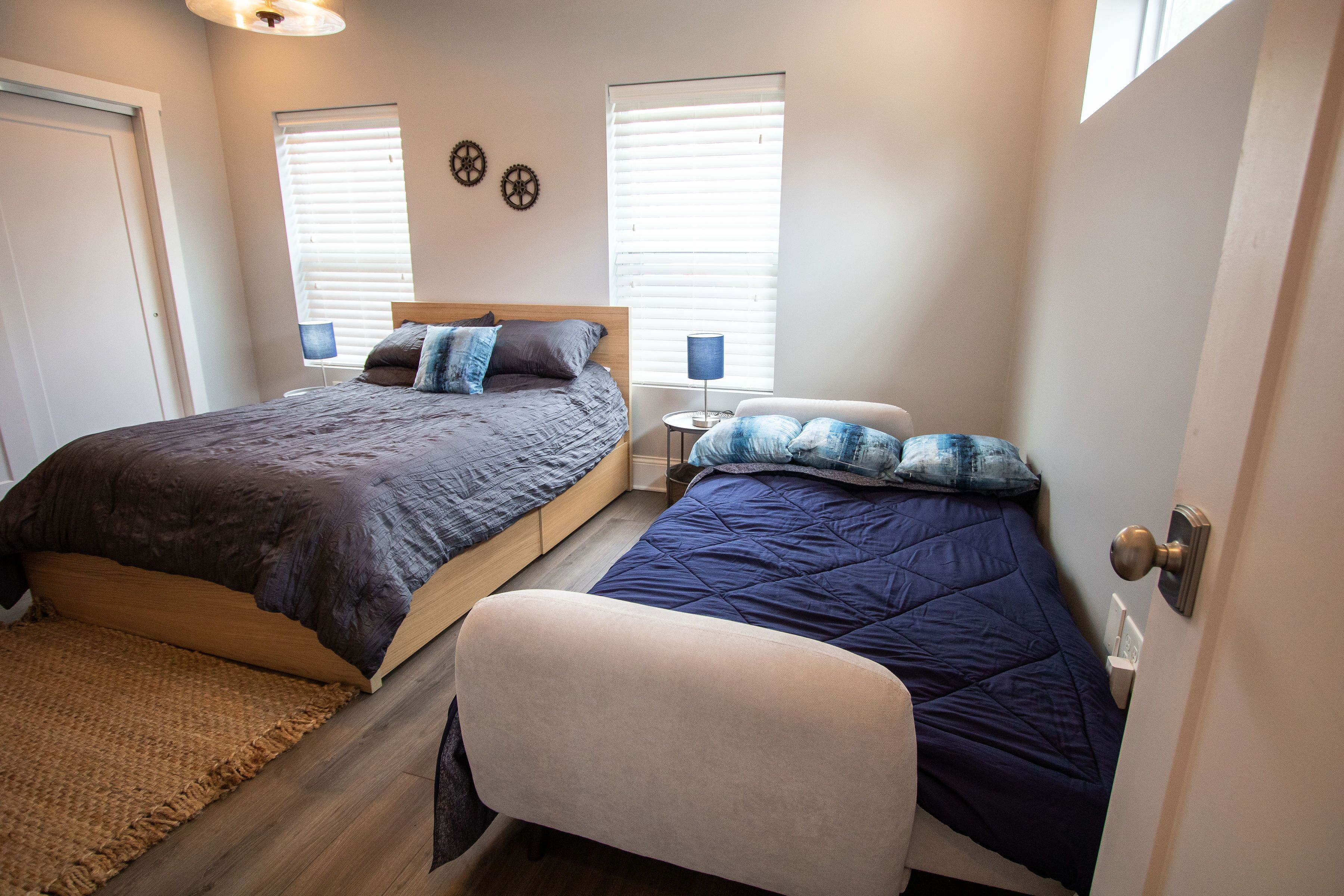 A bedroom with two beds, a small table, and a bench.