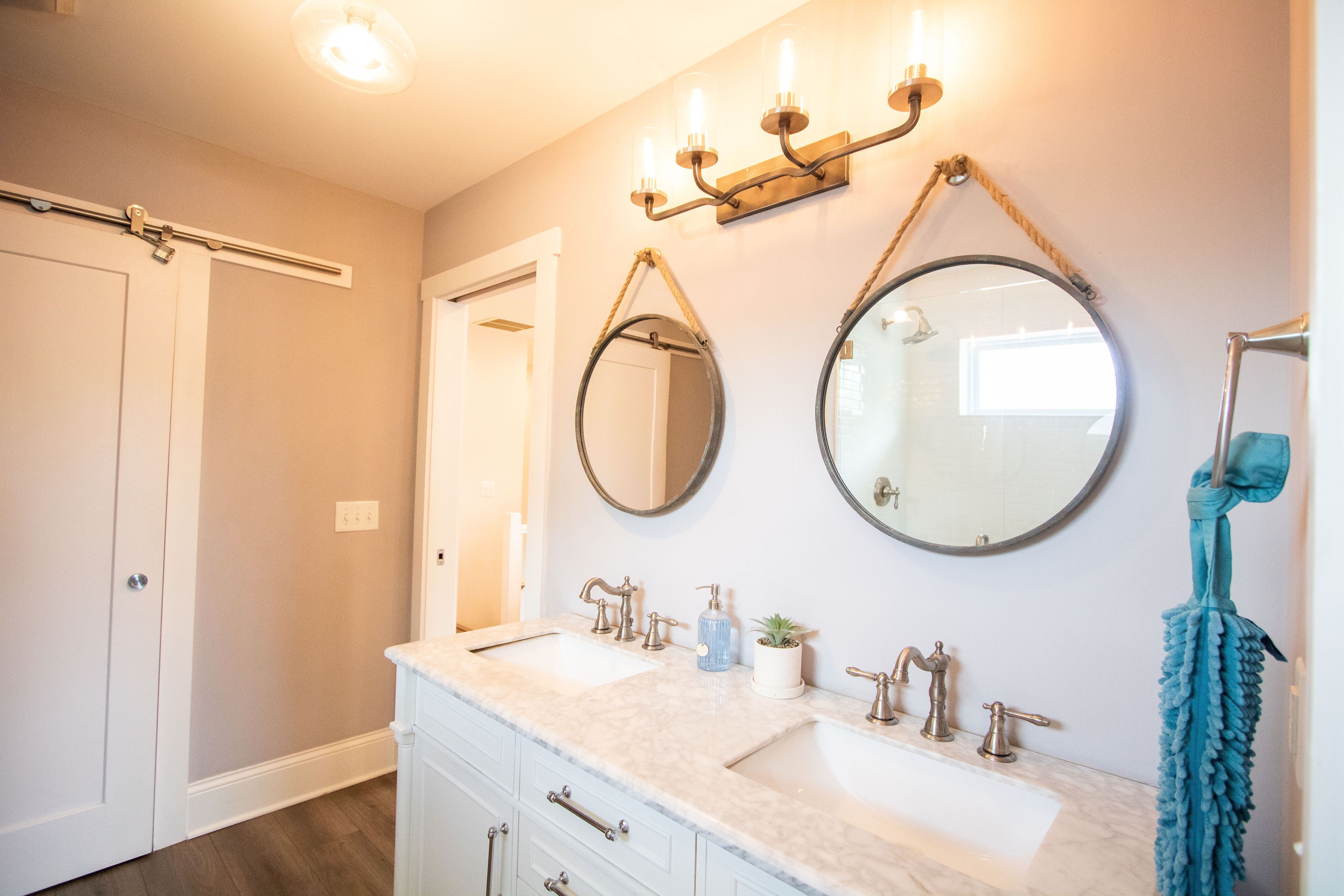 Une salle de bain avec deux lavabos, un miroir, un porte-serviettes et un luminaire.