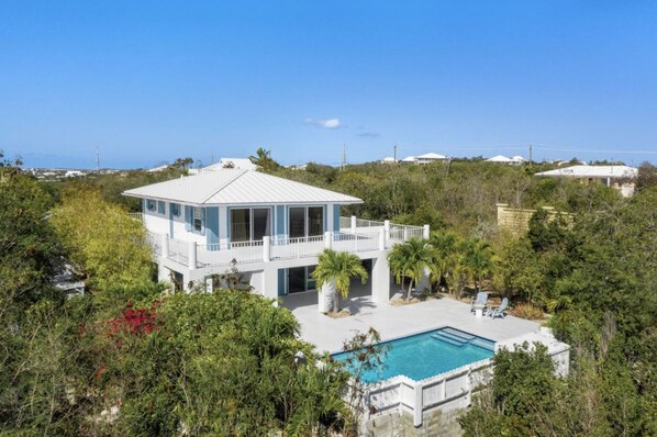 A two-story house with a pool, surrounded by lush greenery and a clear view of the ocean. - Cheerful 3 bedroom Villa close to Grace Bay and Chalk Sound (Blue Mountain)
