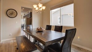 A dining area with a large wooden table, six chairs, a chandelier, and a clock on the wall. - ON THE LAKE Monument & USAFA Mountain View Home. 30 DAY MINIMUM (Monument)
