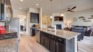 A modern kitchen with dark cabinetry, a central island, and a dining area with a grey sofa. - ON THE LAKE Monument & USAFA Mountain View Home. 30 DAY MINIMUM (Monument)
