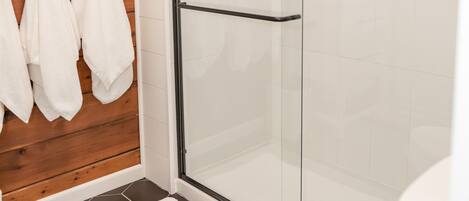 A bathroom with a glass shower enclosure, a white toilet, and a wooden wall with hanging towels.