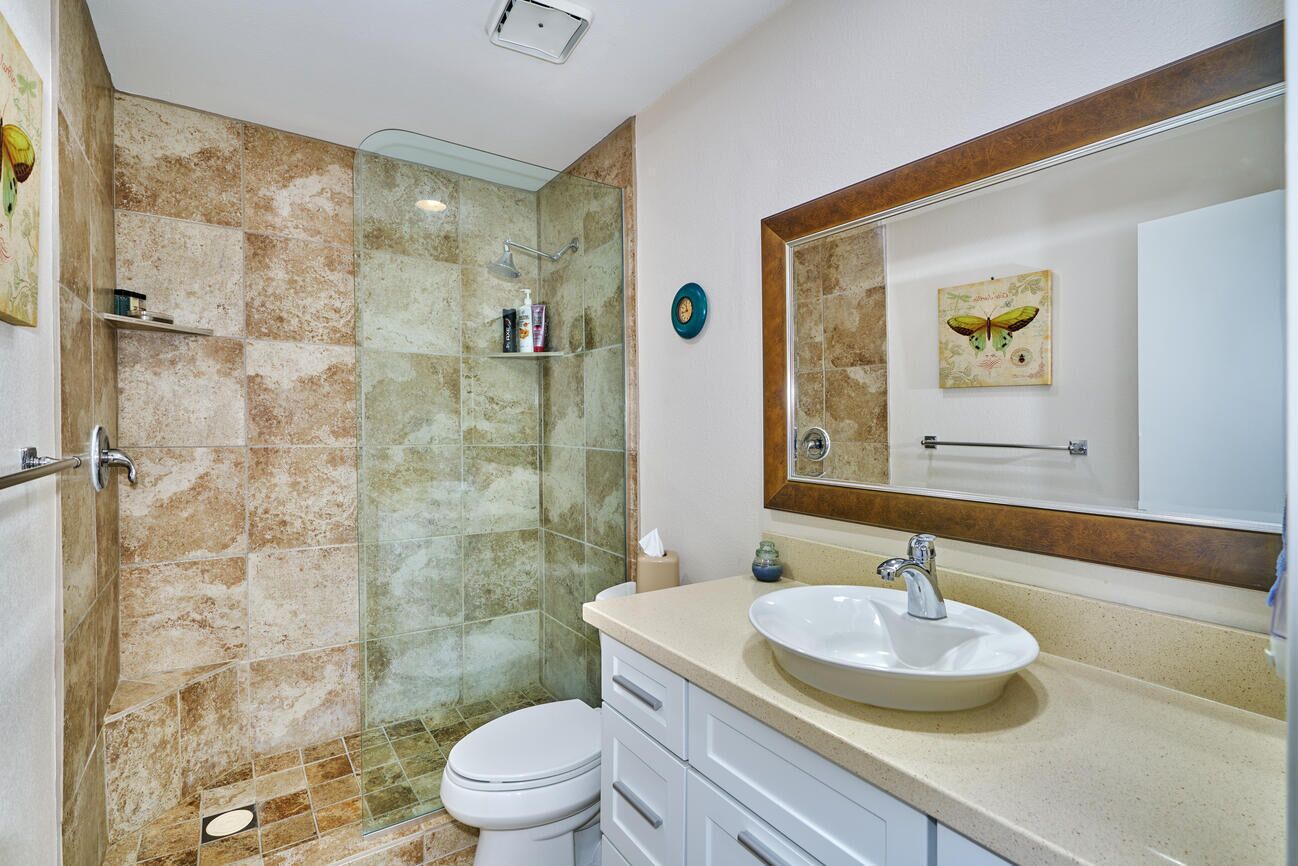 A bathroom with a glass shower enclosure, a white sink, and a large mirror with a butterfly decoration.