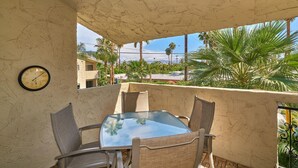 A balcony with a glass table and chairs, a clock on the wall, and a view of palm trees and buildings. - Quaint Palm Springs Condo
City I.D. 032692 (Palm Springs)