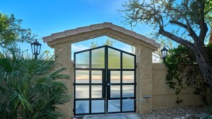 A gated entrance with a stone archway, a glass door, and a concrete pathway leading to a building. - Quaint Palm Springs Condo
City I.D. 032692 (Palm Springs)