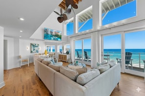 A spacious living room with a large sofa, a television, and a view of the ocean through large windows.