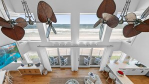 Un vaste espace de vie doté d’une grande fenêtre donnant sur la plage, d’un ventilateur de plafond et d’un coin repas avec vue.