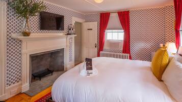 A hotel room with a fireplace, a bed with white bedding, a red and white patterned wall, and a red curtain.