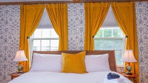 A hotel room with a large bed, yellow curtains, patterned wallpaper, and two bedside lamps.