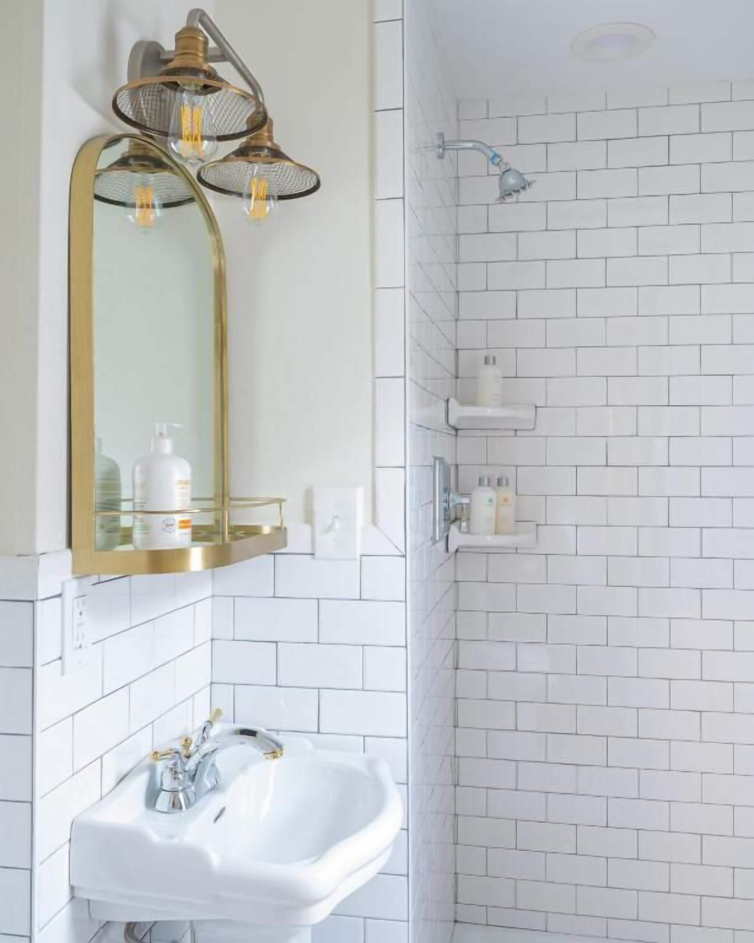 Een badkamer met een wit wastafel, een spiegel met gouden lijst, en een douchegedeelte met witte tegels.