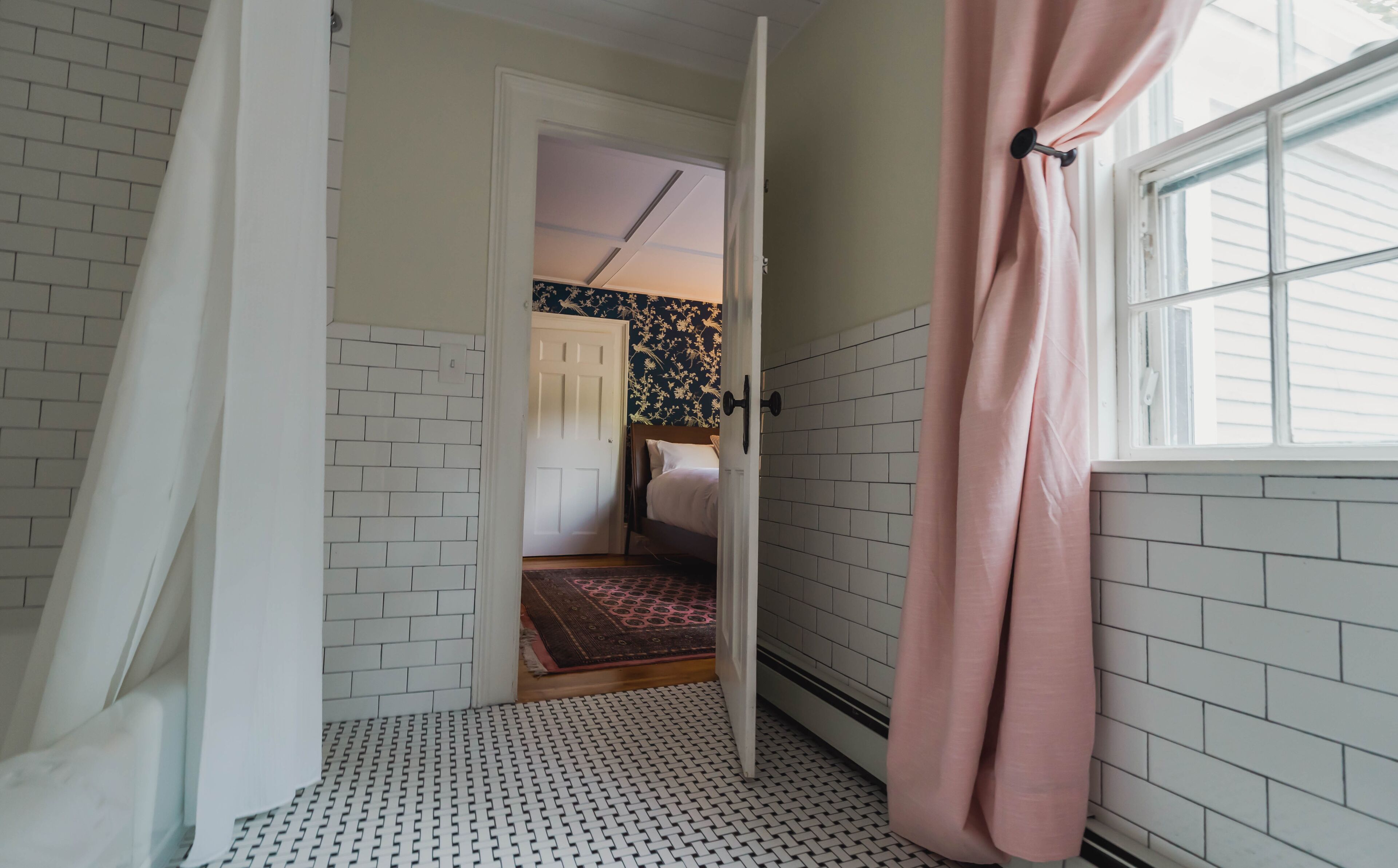 Een kamer met witte bakstenen muren, een kamer met een patroon vloer, een bed met een bloemen hoofdbord en een raam met een gordijn.