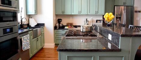 A kitchen with teal cabinets, a granite countertop, stainless steel appliances, and a central island.
