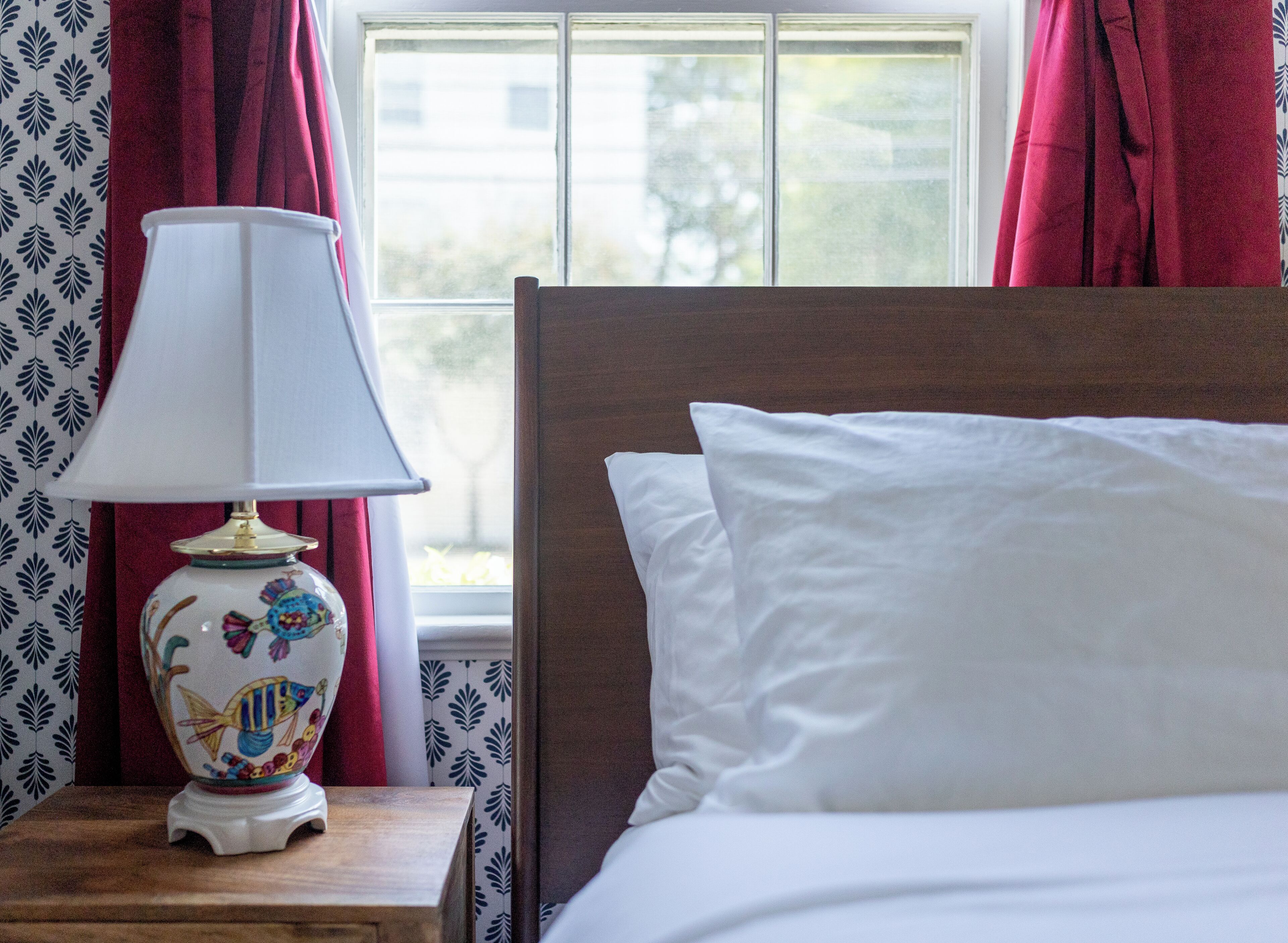 A neatly made bed with white linens, a wooden headboard, and a bedside table with a white lamp featuring a floral design.