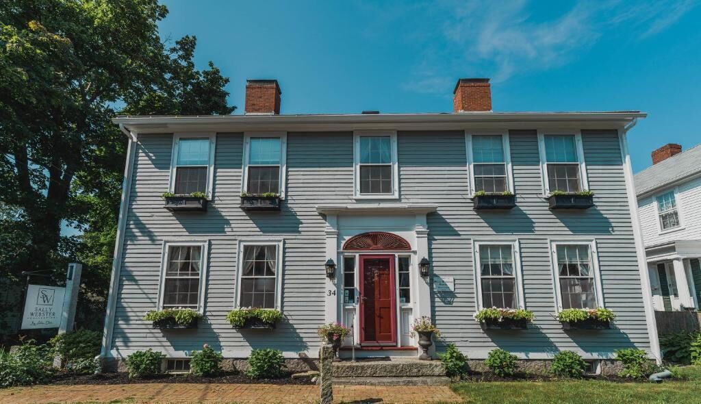 A two-story building with a red door, multiple windows, and flower boxes on the ground floor.