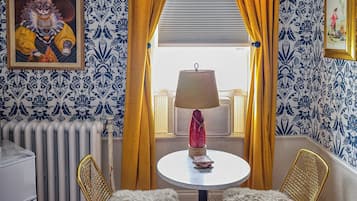 A room with patterned wallpaper, a radiator, a table with a lamp, two chairs, and a red carpet.