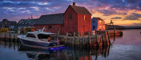A waterfront scene with a docked boat, a red building, and a stone wall.