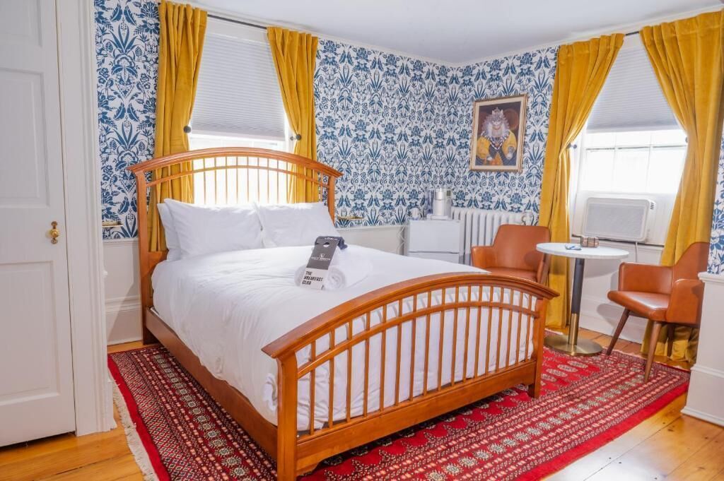 A bedroom with a wooden bed, a red patterned rug, a small round table, and a chair.