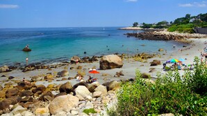 A rocky beach with clear blue water, people sunbathing, and umbrellas.