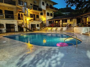 A swimming pool with a pink float, surrounded by lounge chairs and a staircase leading to a balcony.