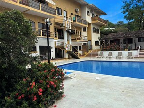 A multi-story building with a swimming pool, outdoor seating, and a staircase leading to a balcony. - Large Central Condo walk to Beach and Restaurants (Tamarindo)