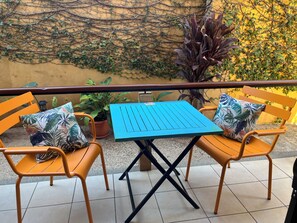 A balcony with two orange chairs, a blue table, and a potted plant.