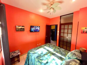 A room with a bed, a television mounted on the wall, and a ceiling fan.