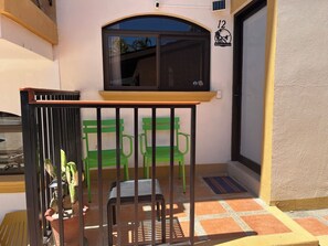 A balcony with a metal railing, a green chair, a potted plant, and a window with a view of palm trees. - Large Central Condo walk to Beach and Restaurants (Tamarindo)