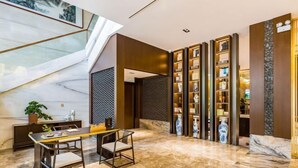 A modern lobby with a marble floor, a dining area with a wooden table and chairs, and a decorative wall with shelves. - Hebei Yeshengyuan Hotel (Pingshan)