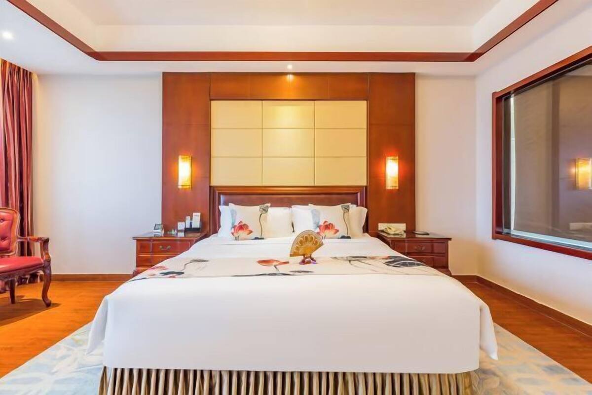 A hotel room with a large bed, wooden headboard, bedside tables, and a large window.