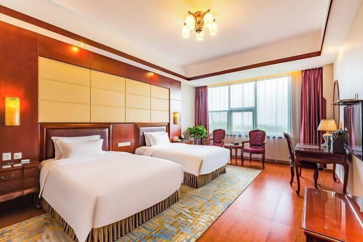 A hotel room with two beds, a desk, a chair, a TV, and a large window.