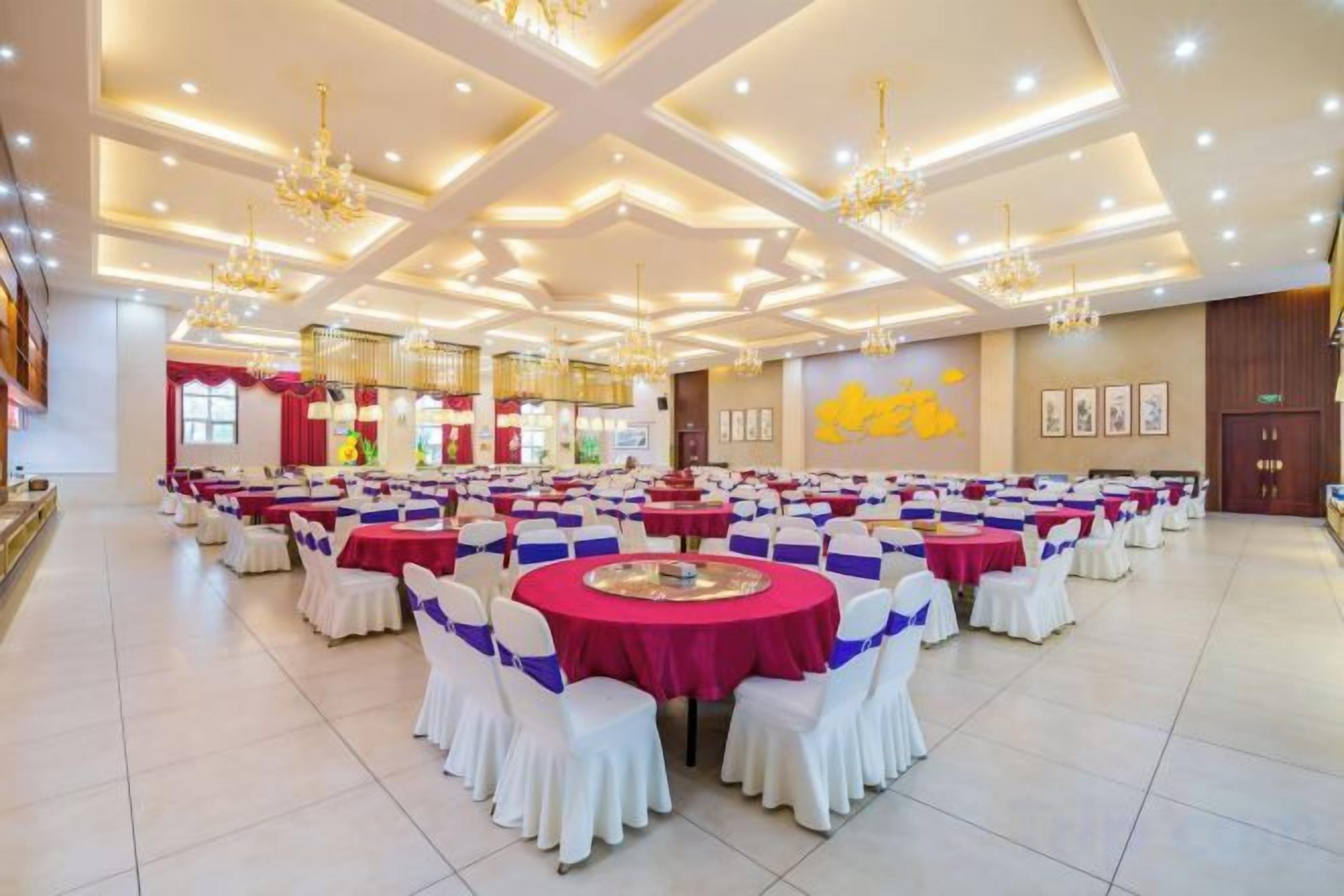 A banquet hall with round tables, white chairs, and chandeliers.
