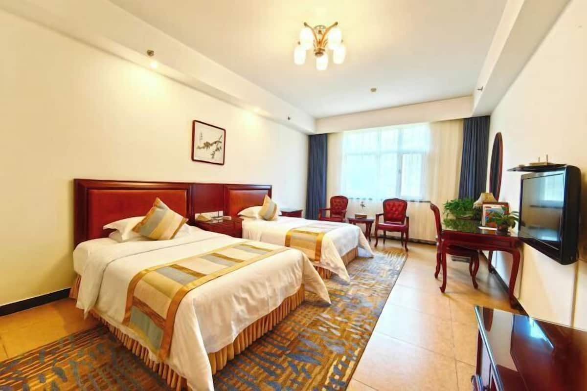 A hotel room with two beds, a desk, a TV, and a large window.