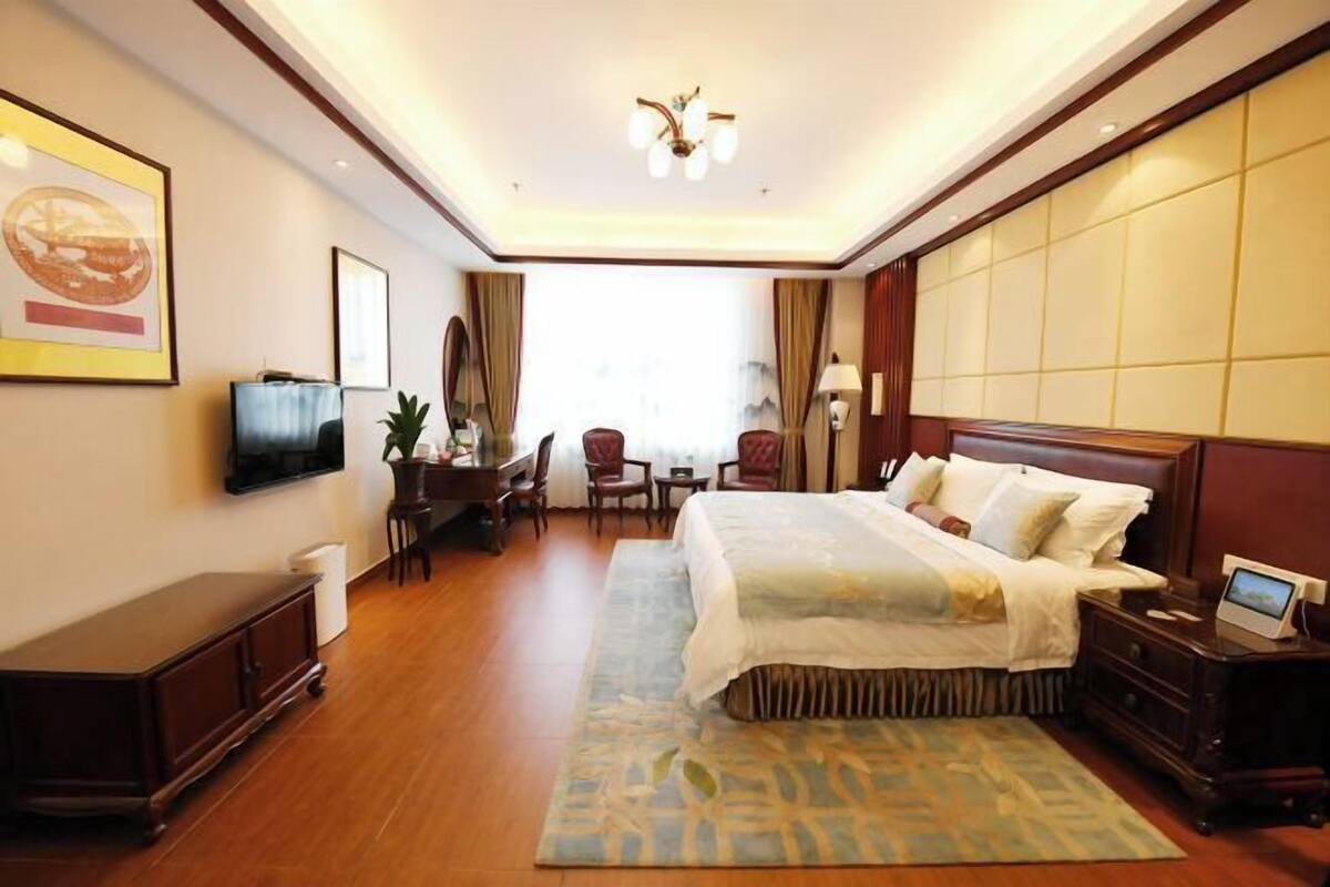 A hotel room with a large bed, a desk with a chair, a television, and a bedside table with a lamp.