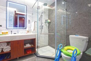 Un baño moderno con ducha de vidrio, inodoro con asiento para niño y tocador con espejo.