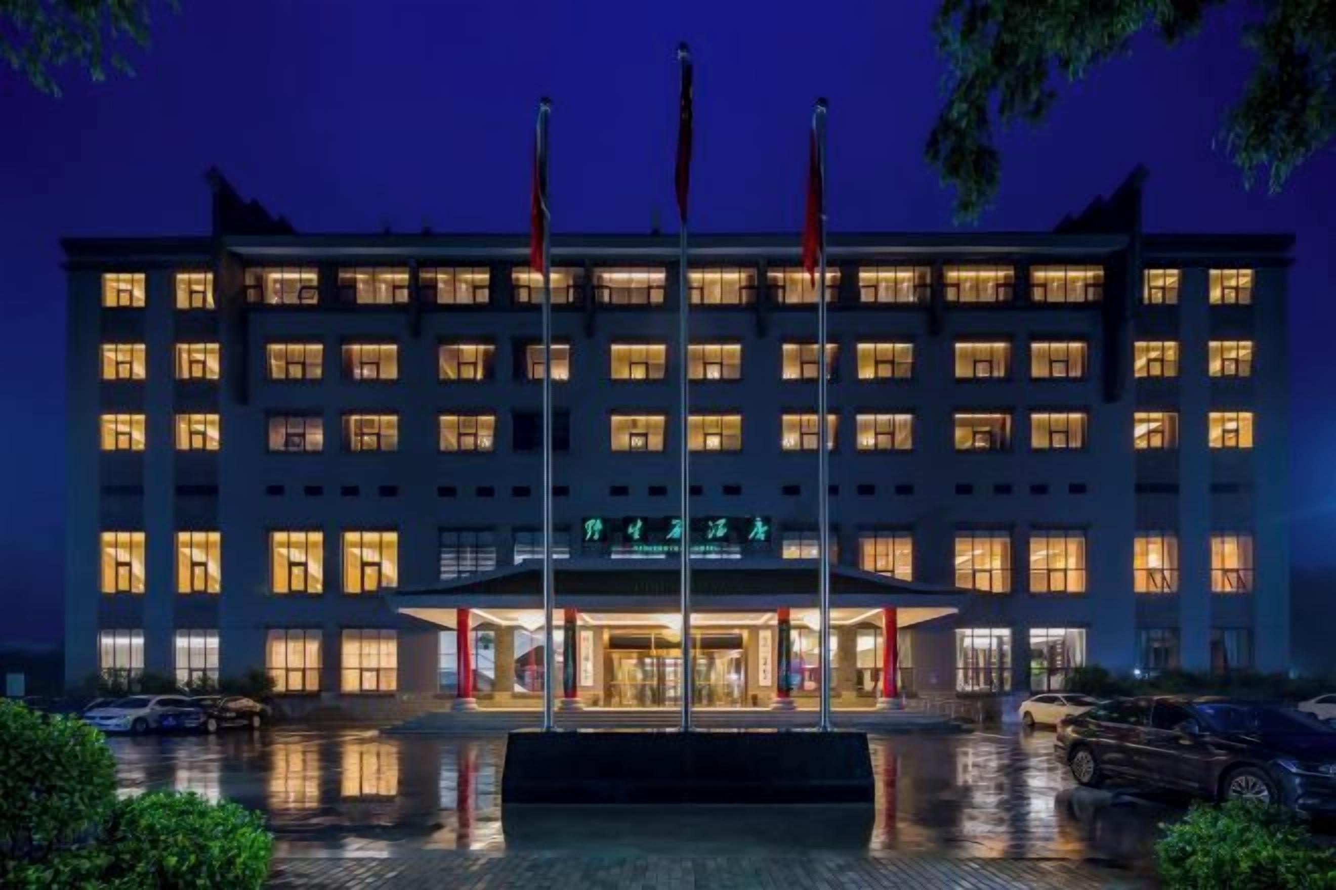 Ein mehrstöckiges Hotel mit gut beleuchtetem Eingang und einem Parkplatz davor.